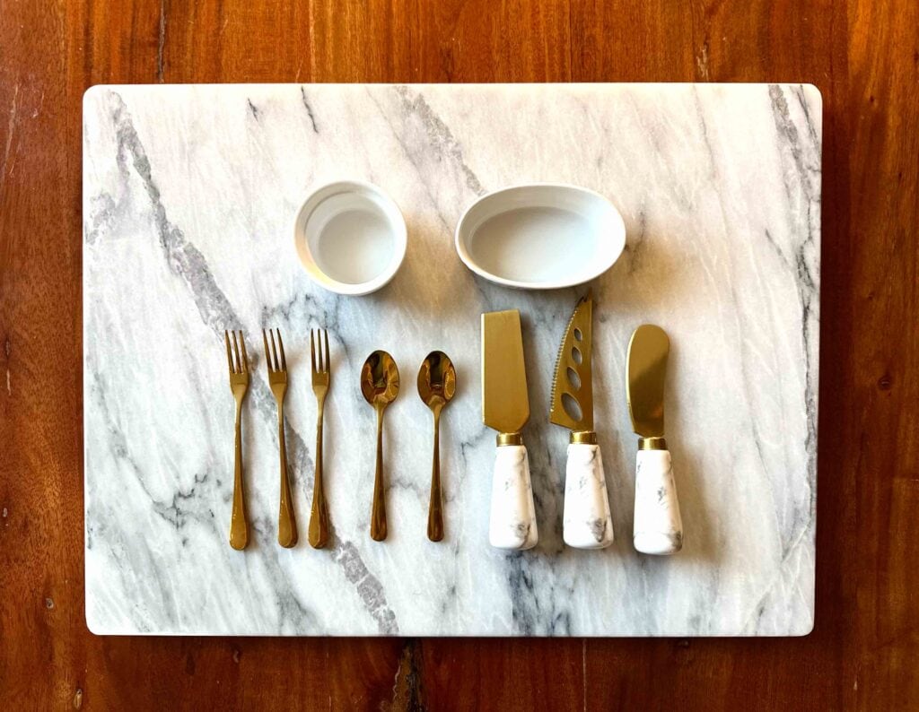 Charcuterie board with cheese knives, forks, spoons, and ramekins