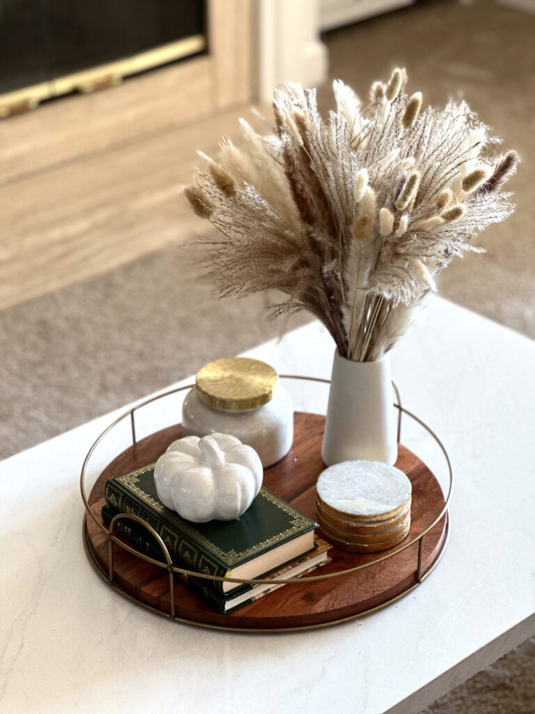 Neutral fall coffee table tray styled with white pumpkin, vintage books, marble coasters, and a vase of dried pampas grass.