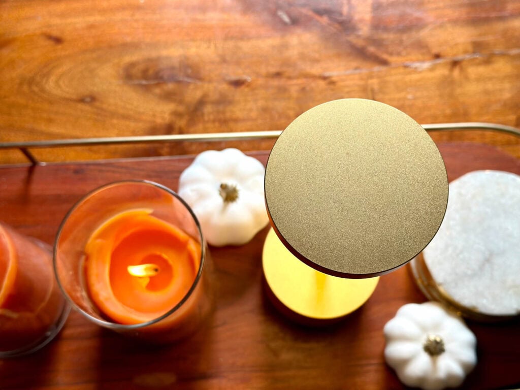 Overhead shot of a fall tray with glowing orange candles, white mini pumpkins, gold LED lamp, and marble coasters on a wood surface.