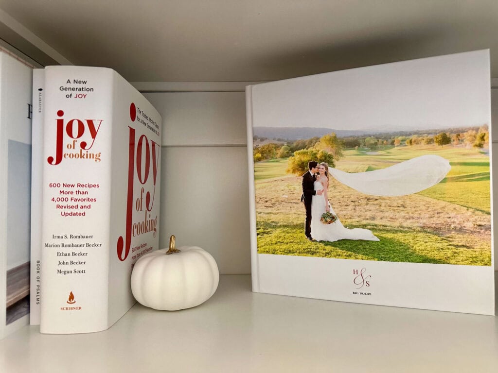 Bookshelf styled with a wedding photo book, the “Joy of Cooking,” and a small white ceramic pumpkin for a subtle fall touch.