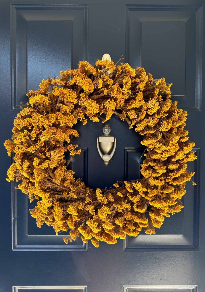 Bright mustard yellow dried floral wreath on a navy blue front door, adding a bold pop of fall color.