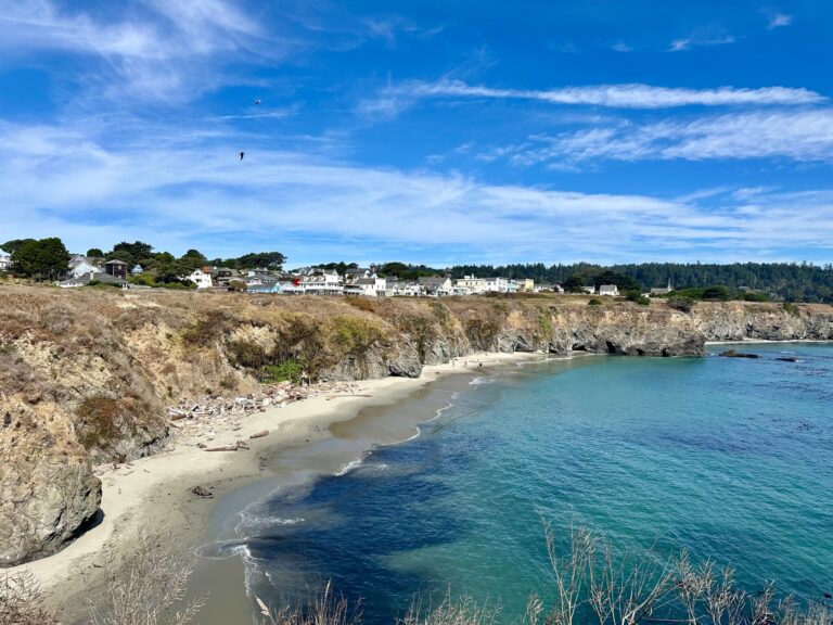 View from a weekend in Mendocino: turquoise water, quiet beach, and cottages along the cliffside
