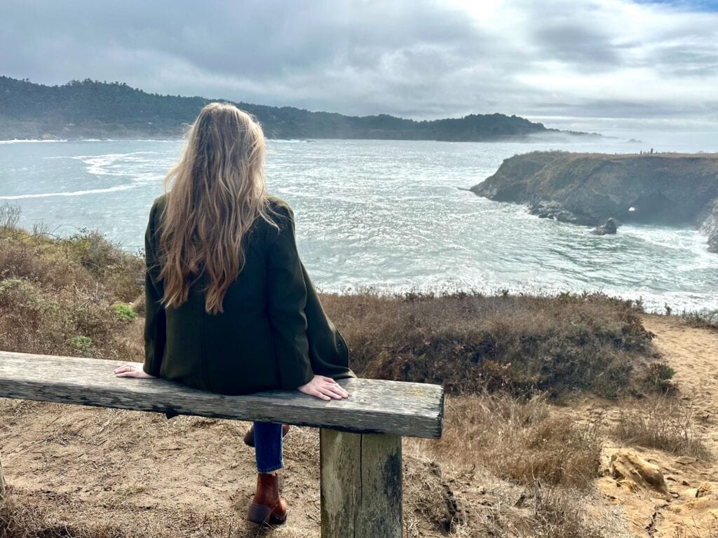 Woman sitting on a wooden bench overlooking cliffs and the Mendocino coast