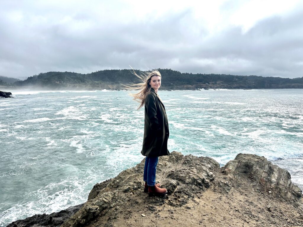 Woman standing on a rocky cliff with waves crashing below in Mendocino