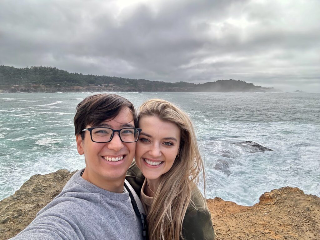 Couple smiling together in front of a rocky coastline and misty ocean backdrop