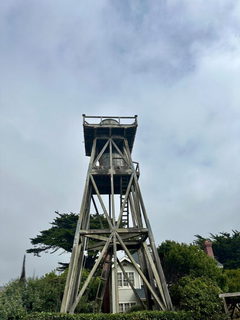 Historic wooden water tower in Mendocino, California, framed by trees and cloudy skies