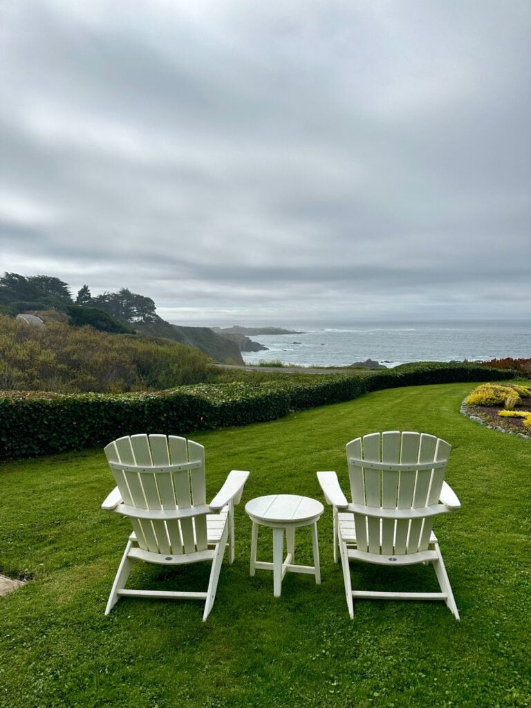 Two white Adirondack chairs facing the ocean on a grassy bluff in Mendocino