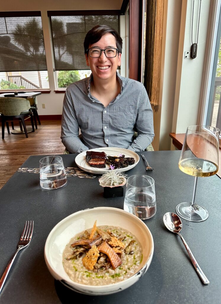 Smiling diner with short rib and risotto entrees at a window table in Mendocino