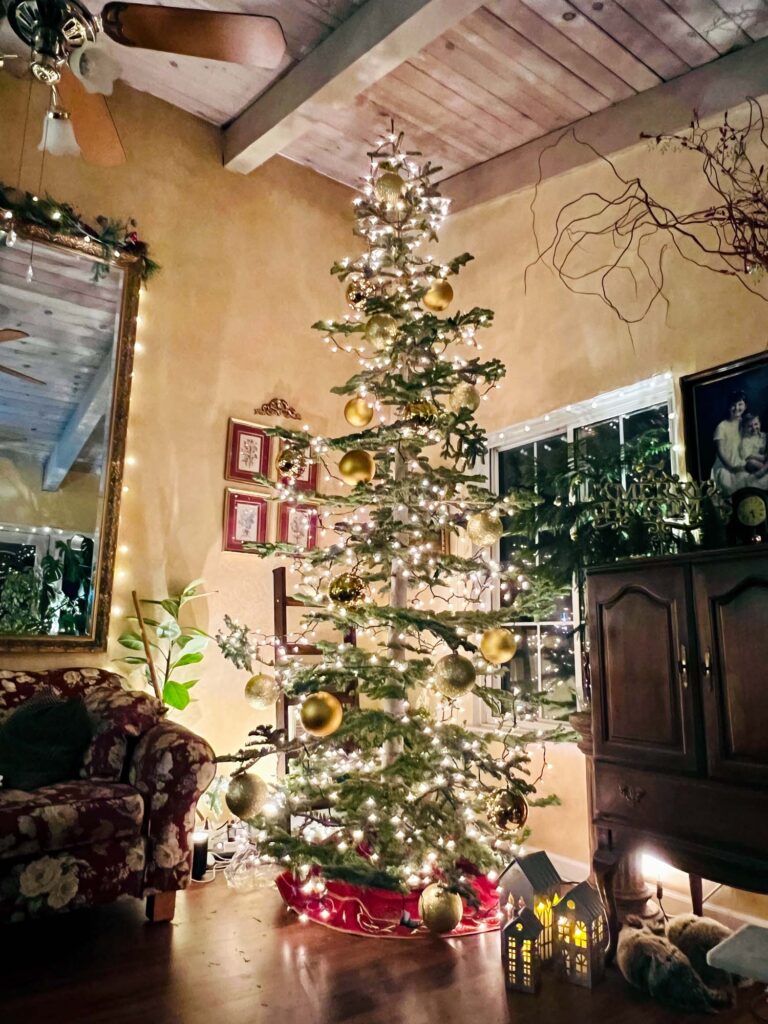 Silvertip Christmas tree decorated with lights and large gold ball ornaments in low-lit living room