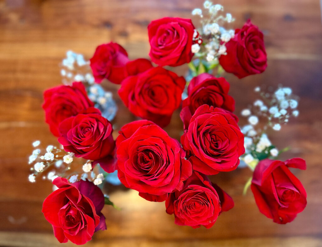 Close-up of red roses with baby’s breath arranged on a wooden table for a Bachelor-themed party