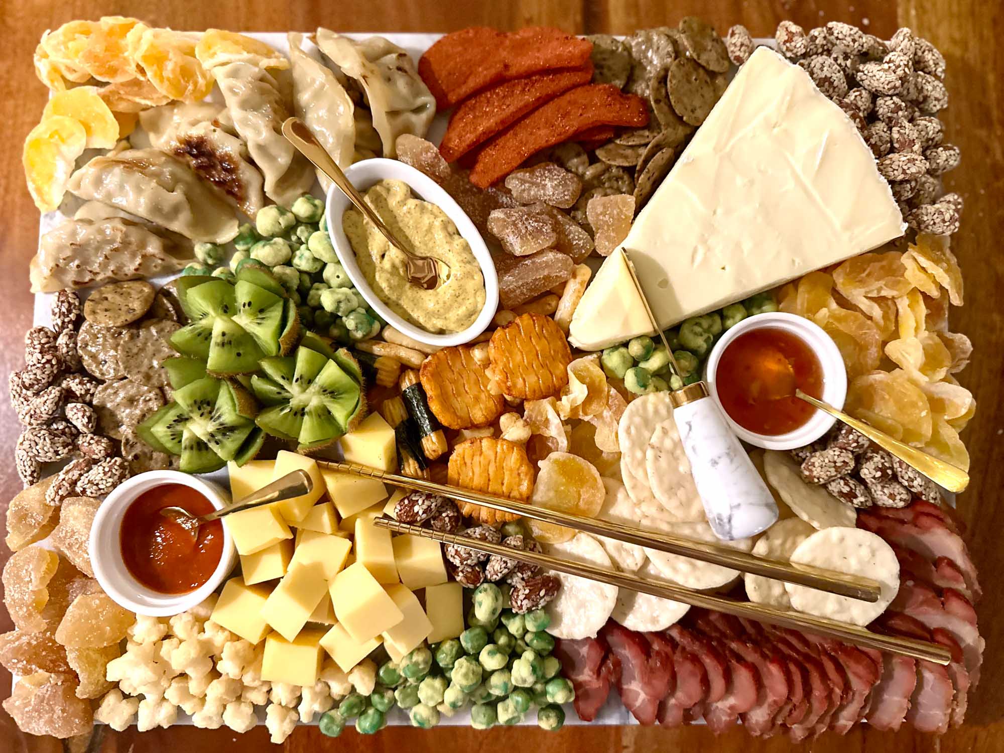 Asian charcuterie board featuring brie with chili sauce, char siu, and rice crackers