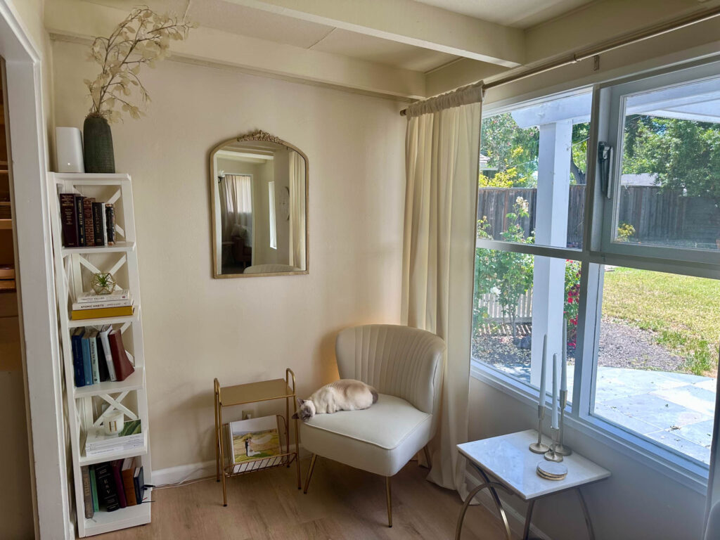 Cozy rental living space with a white accent chair, bookshelf, and natural light—styled with renter-friendly decor that adds personality without damage.