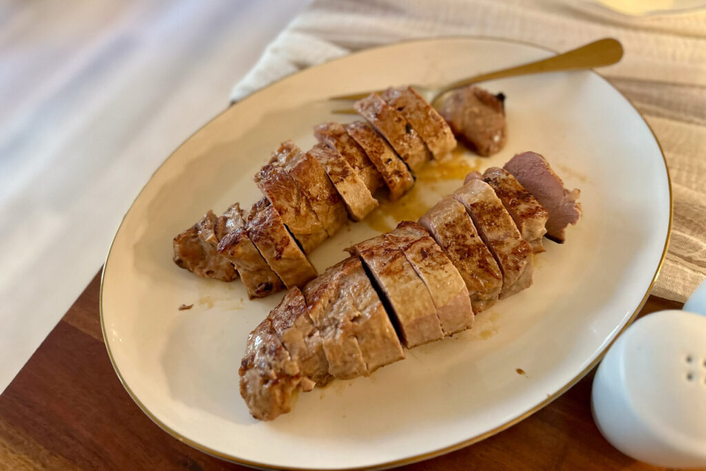 Sliced pork tenderloin arranged neatly on a white plate with a gold-rim edge, ready to serve