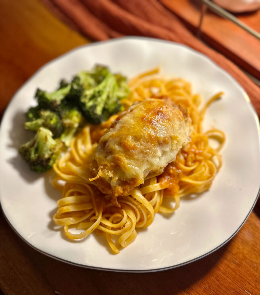 Plate of linguine tossed in Trader Joe’s Autumnal Harvest pasta sauce, topped with breaded chicken parmesan and roasted broccoli.