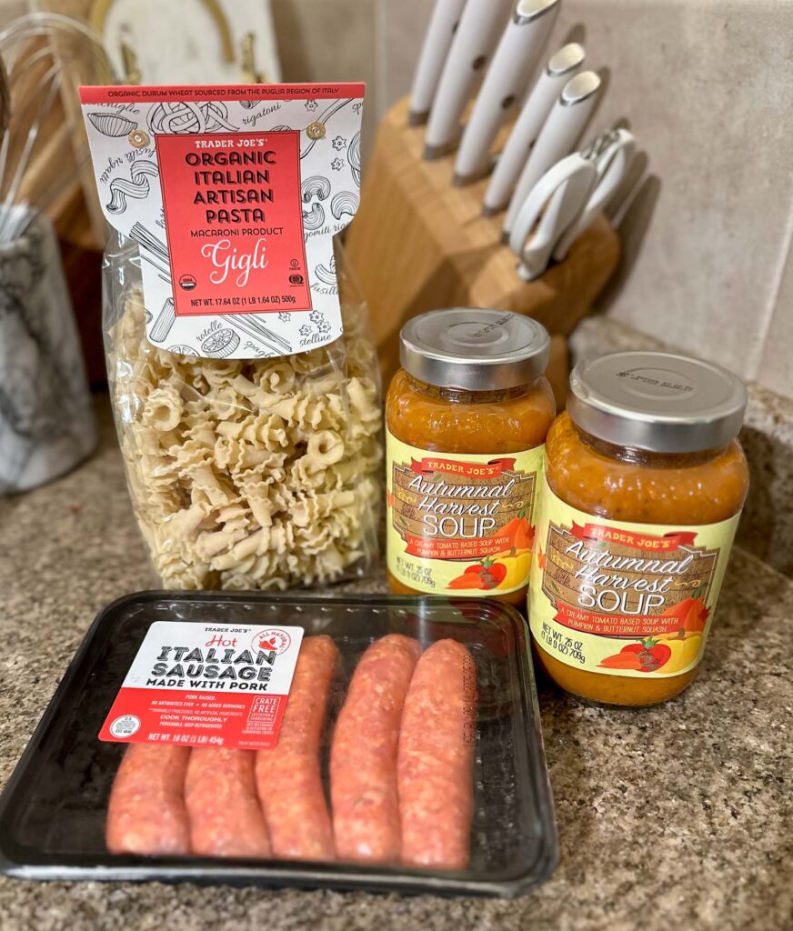 Trader Joe’s Autumnal Harvest Soup jars, hot Italian sausage, and artisan pasta displayed on a kitchen counter.