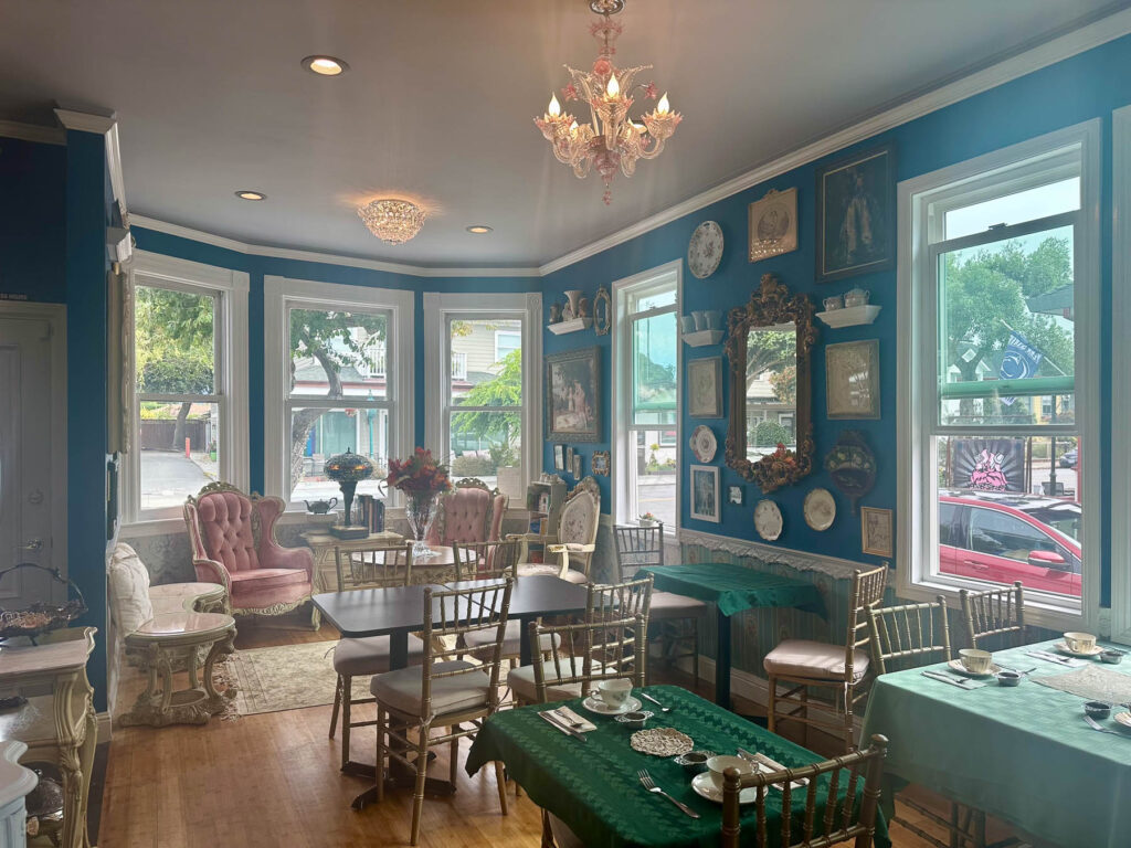 Elegant Victorian-style tea room interior with teal walls, gold-framed mirrors, vintage furniture, and multiple tables set for afternoon tea at By the Teashore in Half Moon Bay.