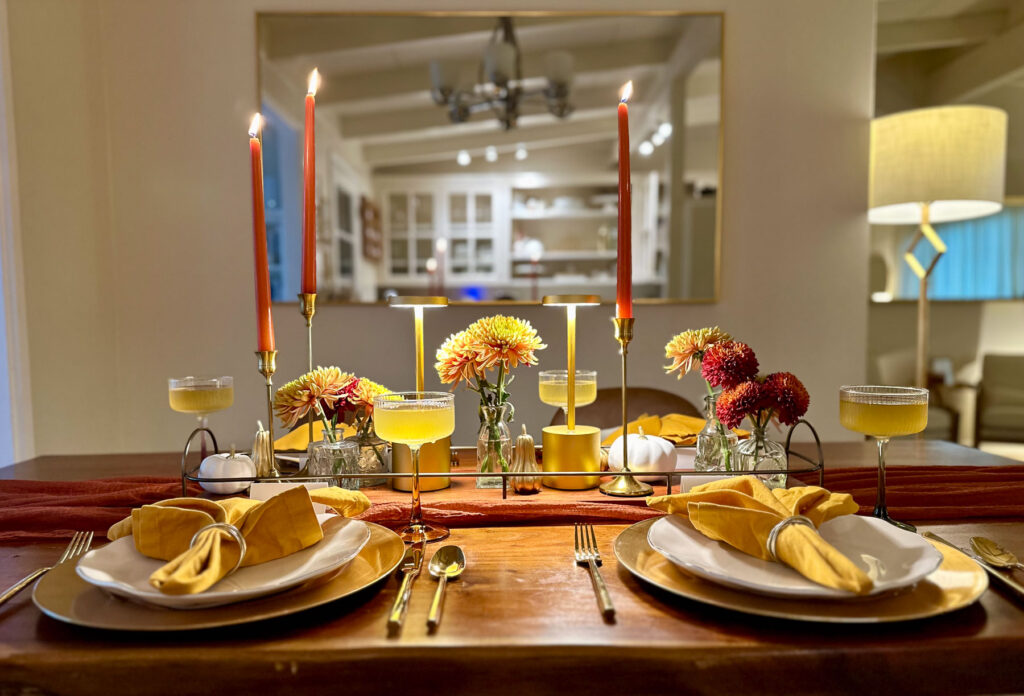 Warm autumn tablescape with candles, mums, coupe glasses, and gold-accented place settings for a fall dinner party.