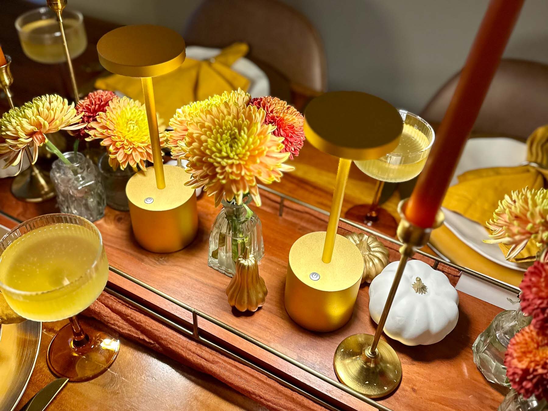 Bud vases filled with golden mums styled alongside modern gold downlights on a fall dinner table.