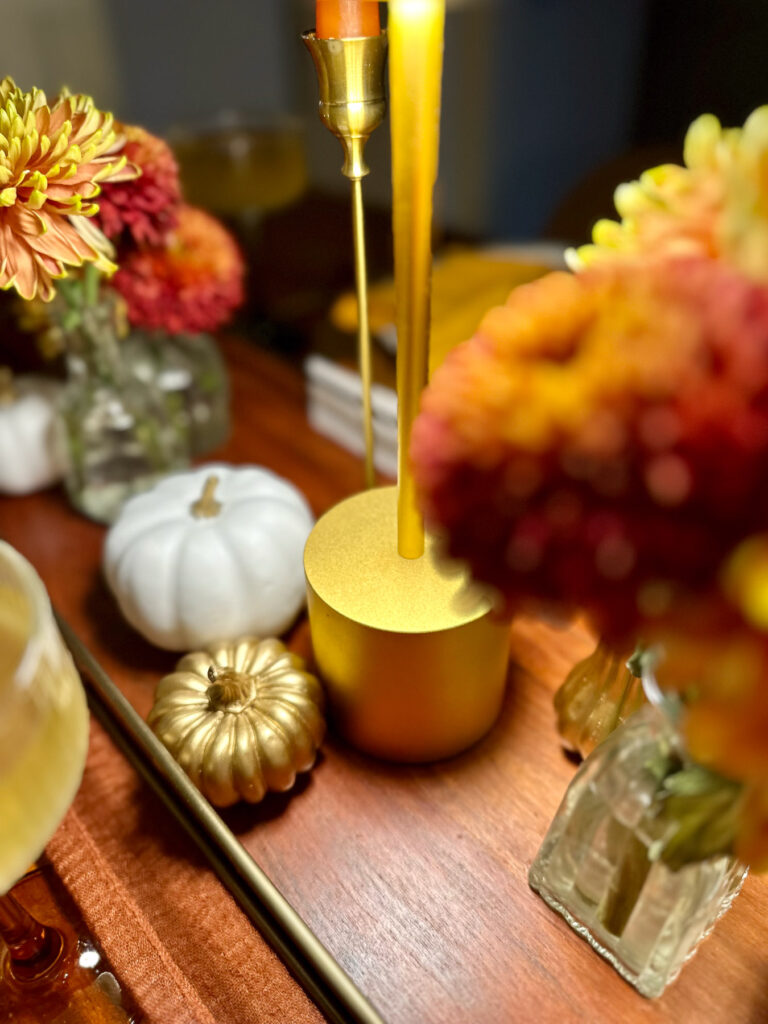 Close-up of centerpiece decor featuring gold and white mini pumpkins, gold downlight, and fall mums in glass bud vases.