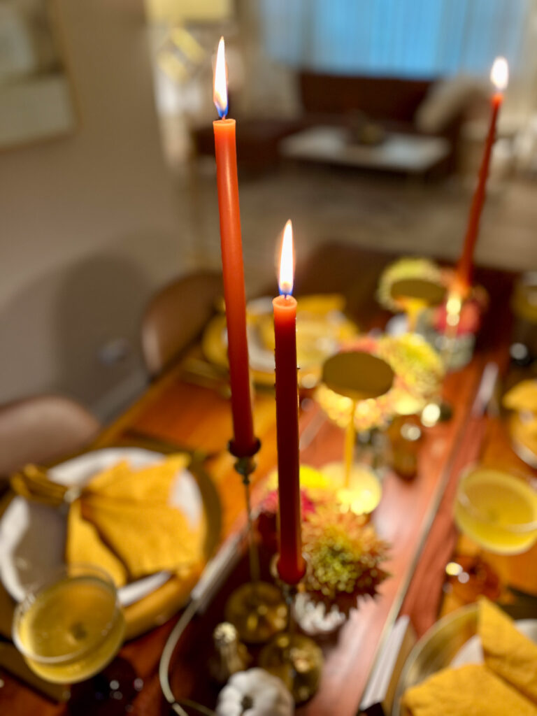 Burnt orange taper candles in gold candlesticks glowing above a fall dinner party table.