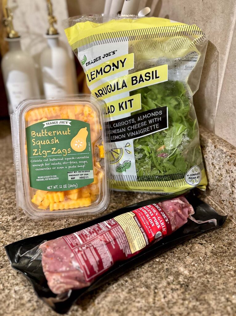 Trader Joe’s butternut squash zig-zags, lemony arugula basil salad kit, and peppercorn-garlic pork tenderloin on a counter.