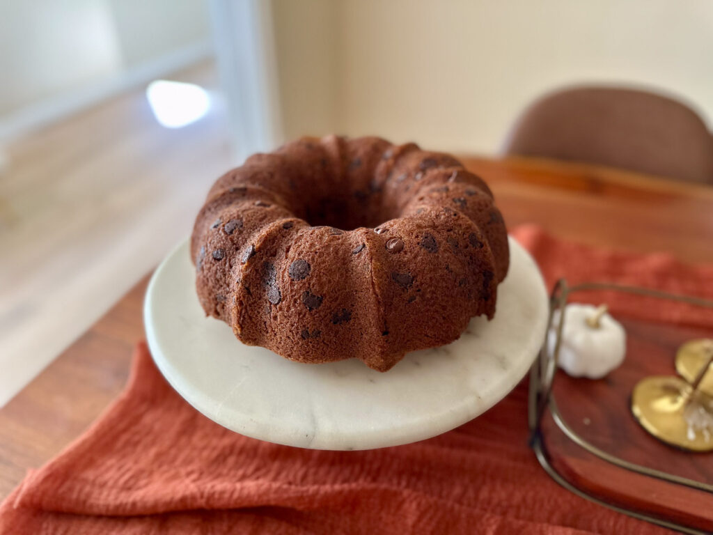 Pumpkin chocolate chip Bundt cake on a white marble cake stand with a rust-colored linen underneath.