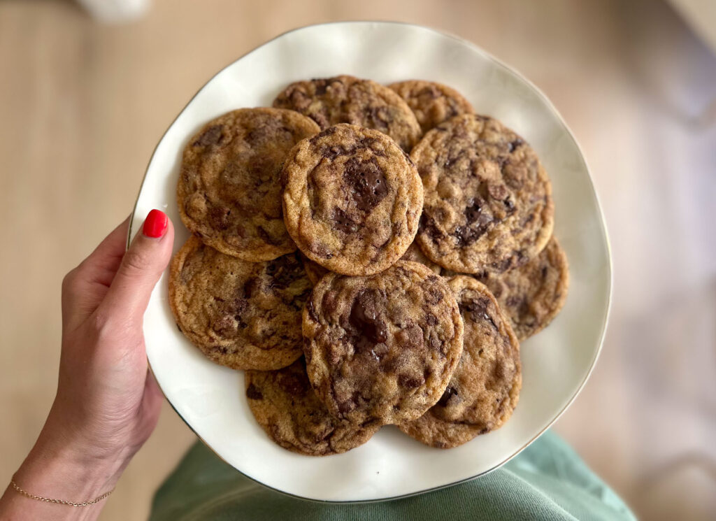 Plate of pumpkin butter chocolate chip cookies held in one hand, showing melty chunks of dark chocolate.