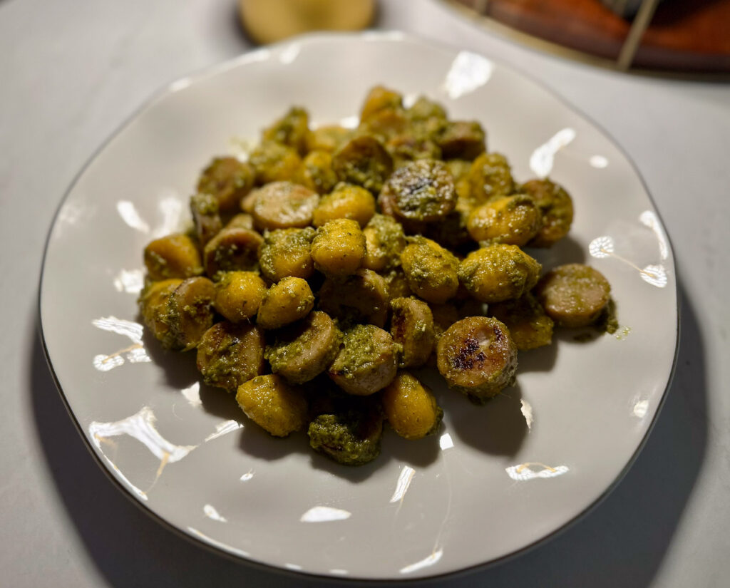 Plate of pumpkin gnocchi and chicken apple sausage coated in basil pesto.