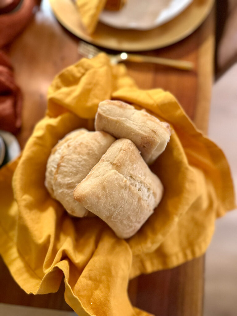 Basket of dinner rolls wrapped in an ochre napkin, styled on a fall dinner party table.