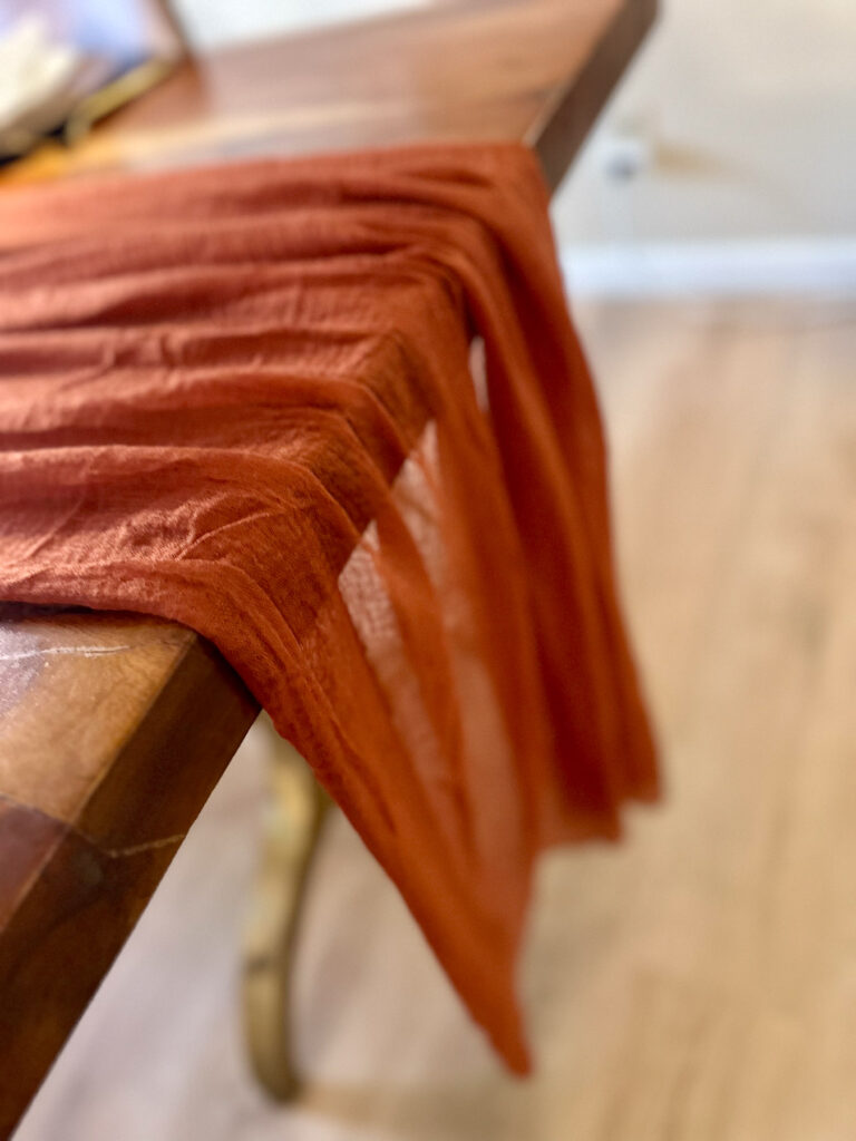 Terracotta gauze table runner draped across a wooden dining table for autumn entertaining.