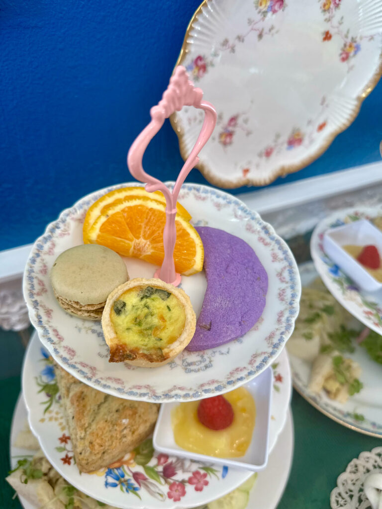 Close-up of the top tier of the afternoon tea tray, featuring quiche, macaron, orange slices, and a lavender cookie.