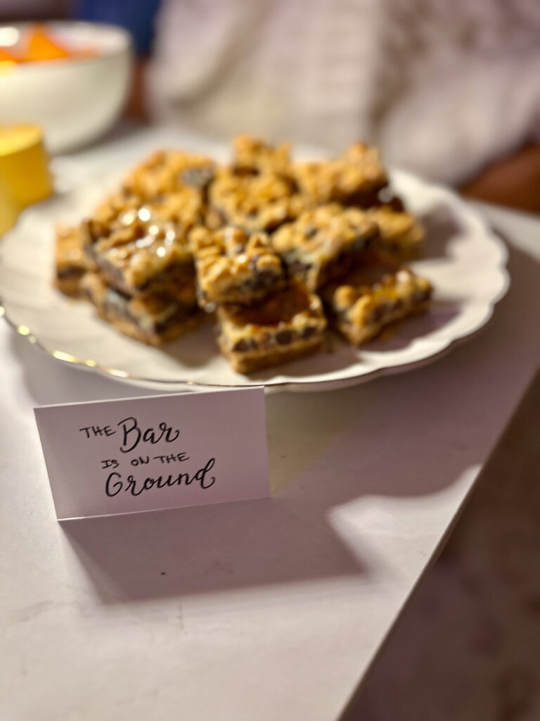 Plate of five-layer magic bar cookies with a card reading “The Bar Is on the Ground."