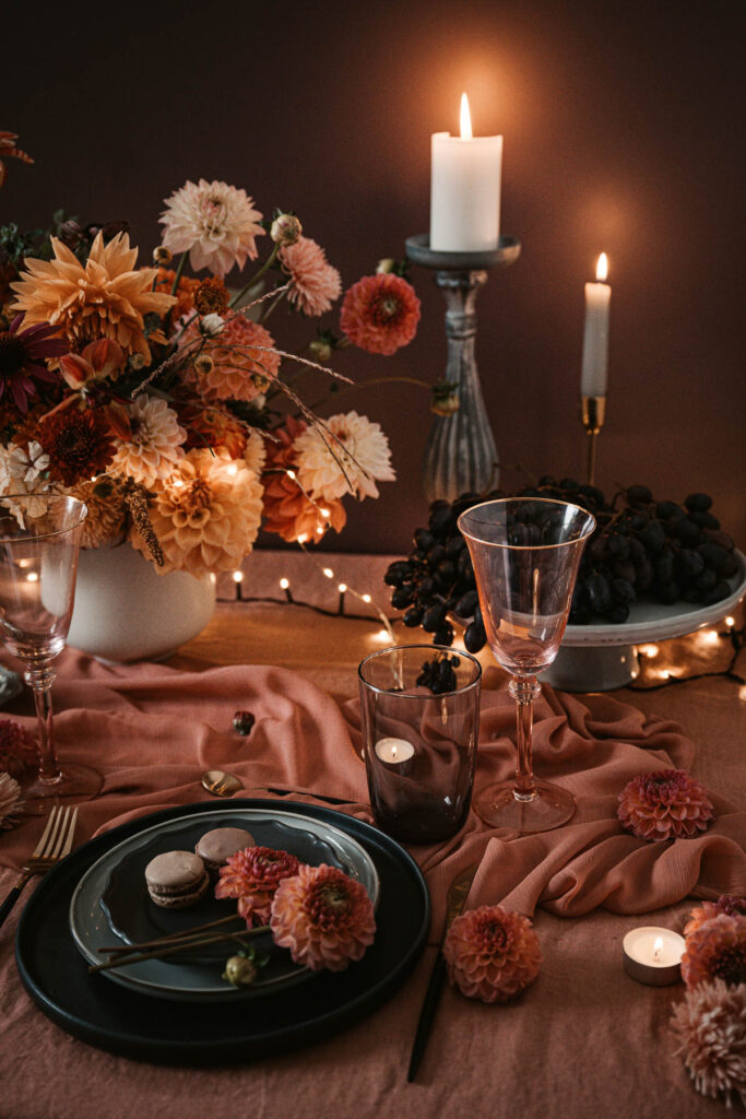 Moody fall dinner table with dahlias, candles, and amber lighting — elegant tablescape inspiration for hosting a sophisticated Halloween or harvest party.