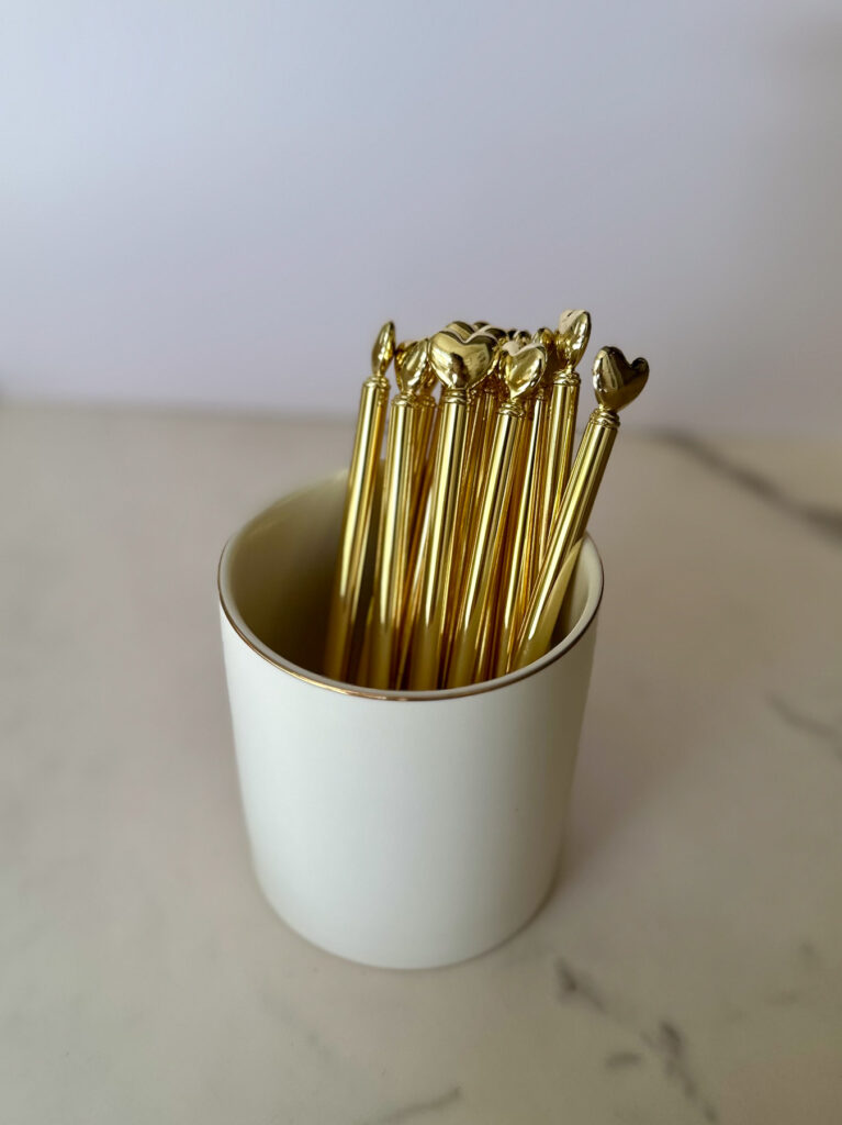 Gold heart-topped pens in a white cup for journaling during a Love Is Blind watch party.