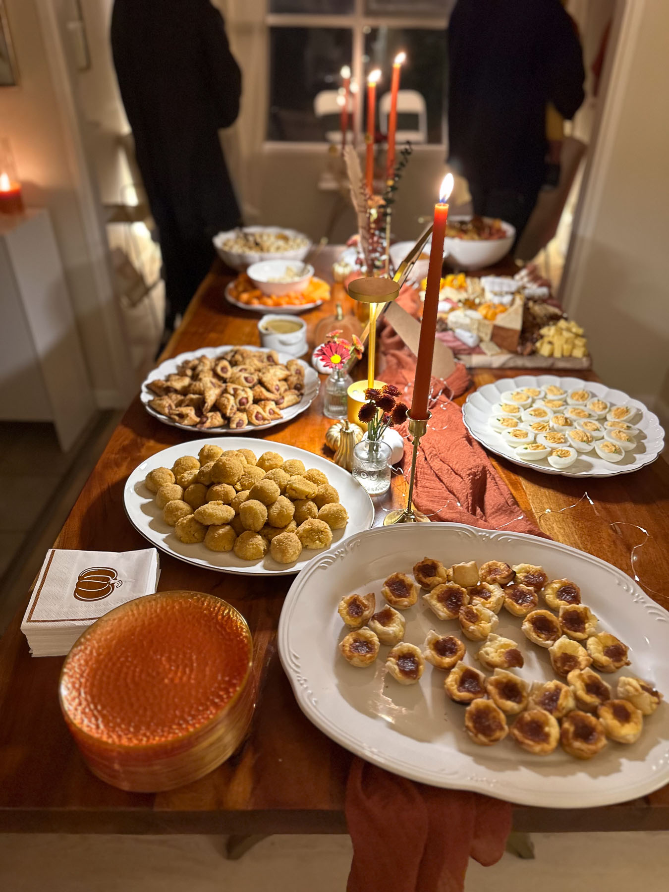 A full bird's-eye view looking down a long wooden dining table crowded with platters of Halloween appetizers, deviled eggs, and fall party food under warm lighting.