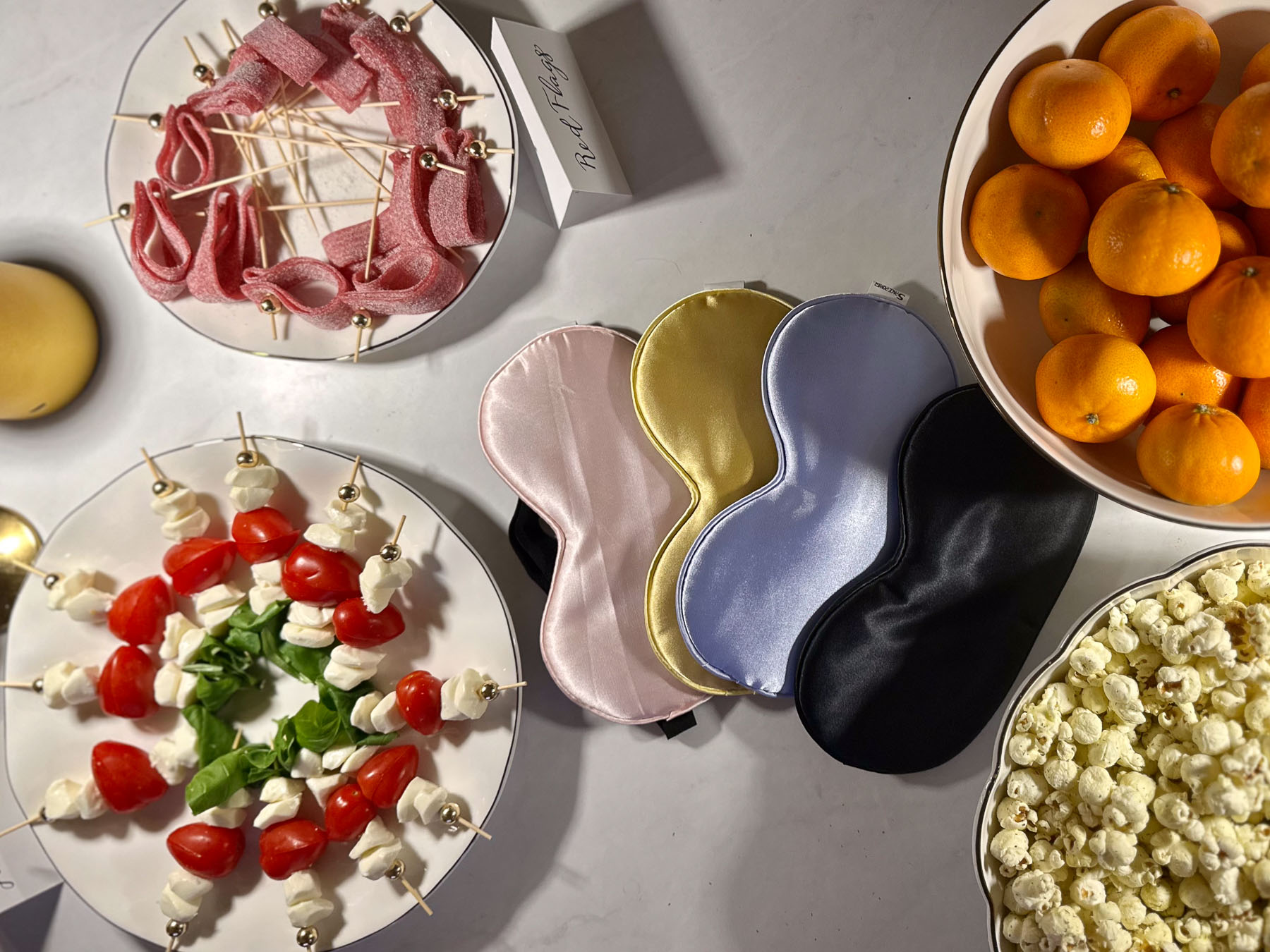 Love Is Blind watch party setup with silk eye masks, caprese skewers, popcorn, and tangerines on a marble table.