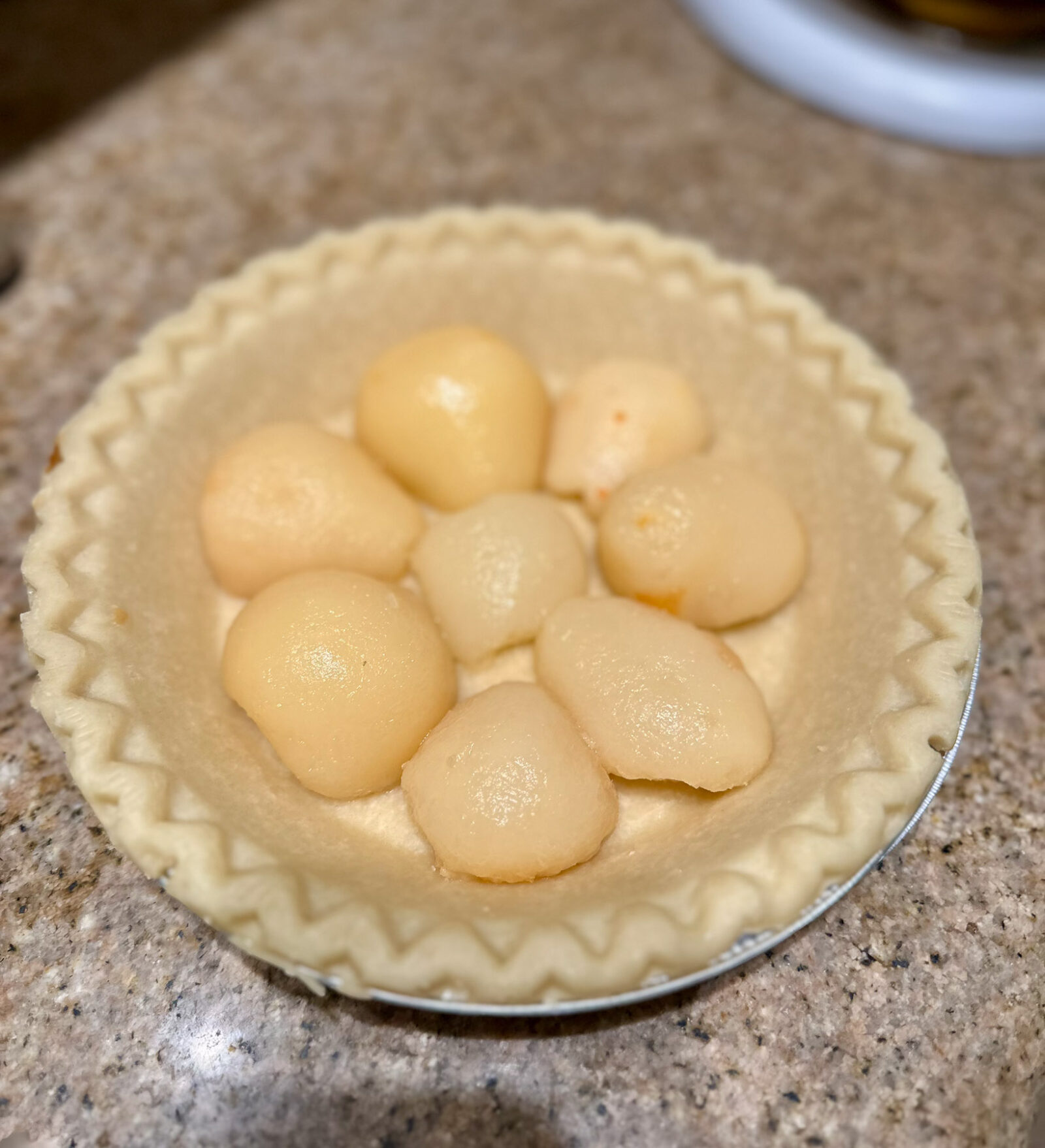 Pie shell filled with pear halves arranged evenly for the pear pie base.