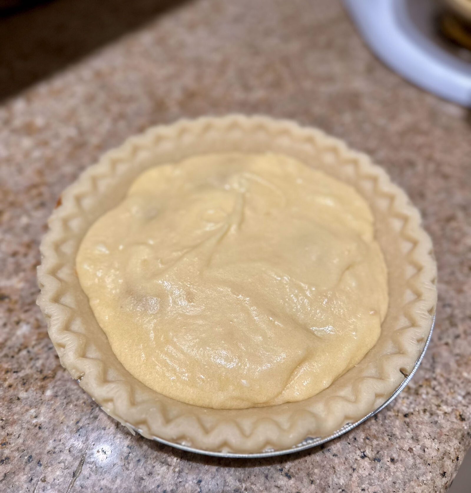 Unbaked pear pie topped with smooth, golden batter before baking.