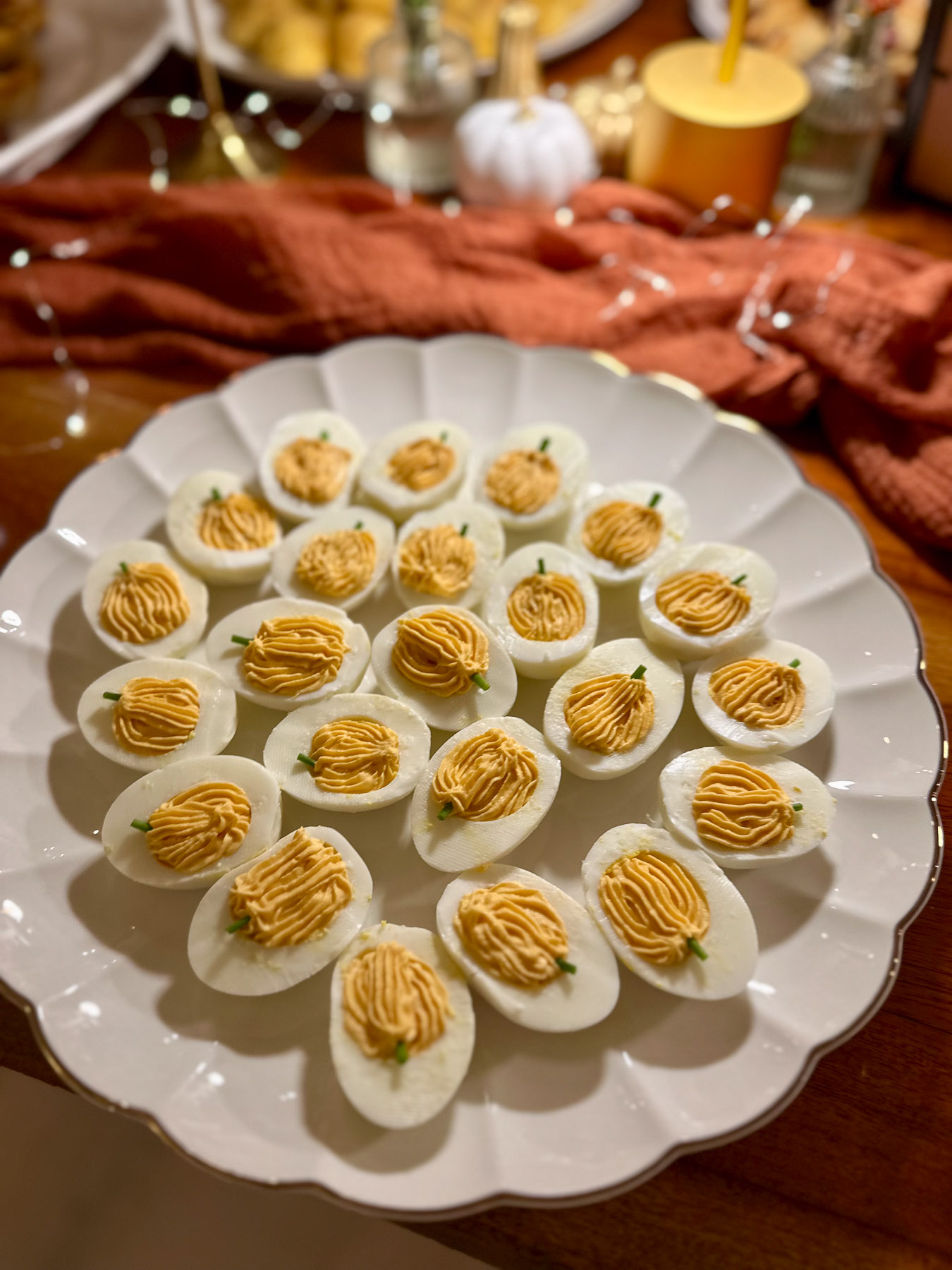 A scalloped white platter filled with Halloween deviled eggs piped and styled with tiny chives to look like miniature pumpkins.