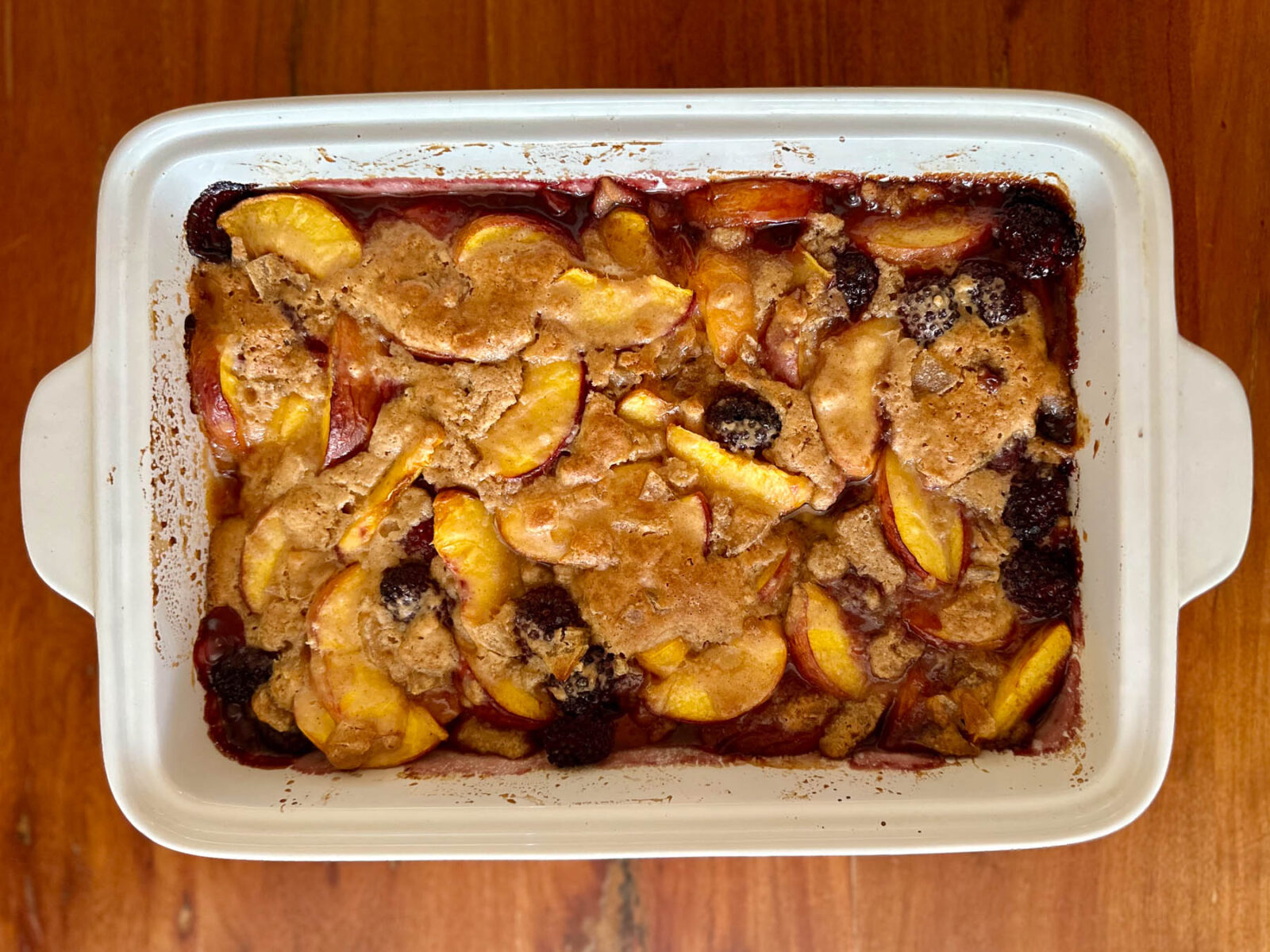 Ginger blackberry peach cobbler baked in a white casserole dish with a bubbling fruit filling.