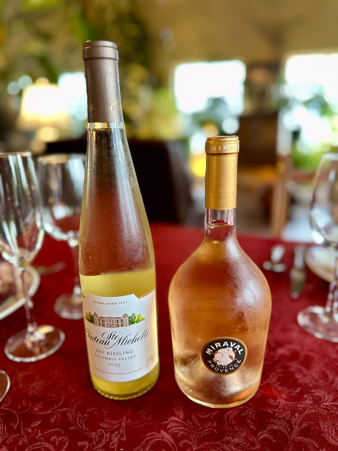 Chateau Ste. Michelle dry riesling and Miraval Côtes de Provence rosé bottles with condensation on a red tablecloth during tasting.