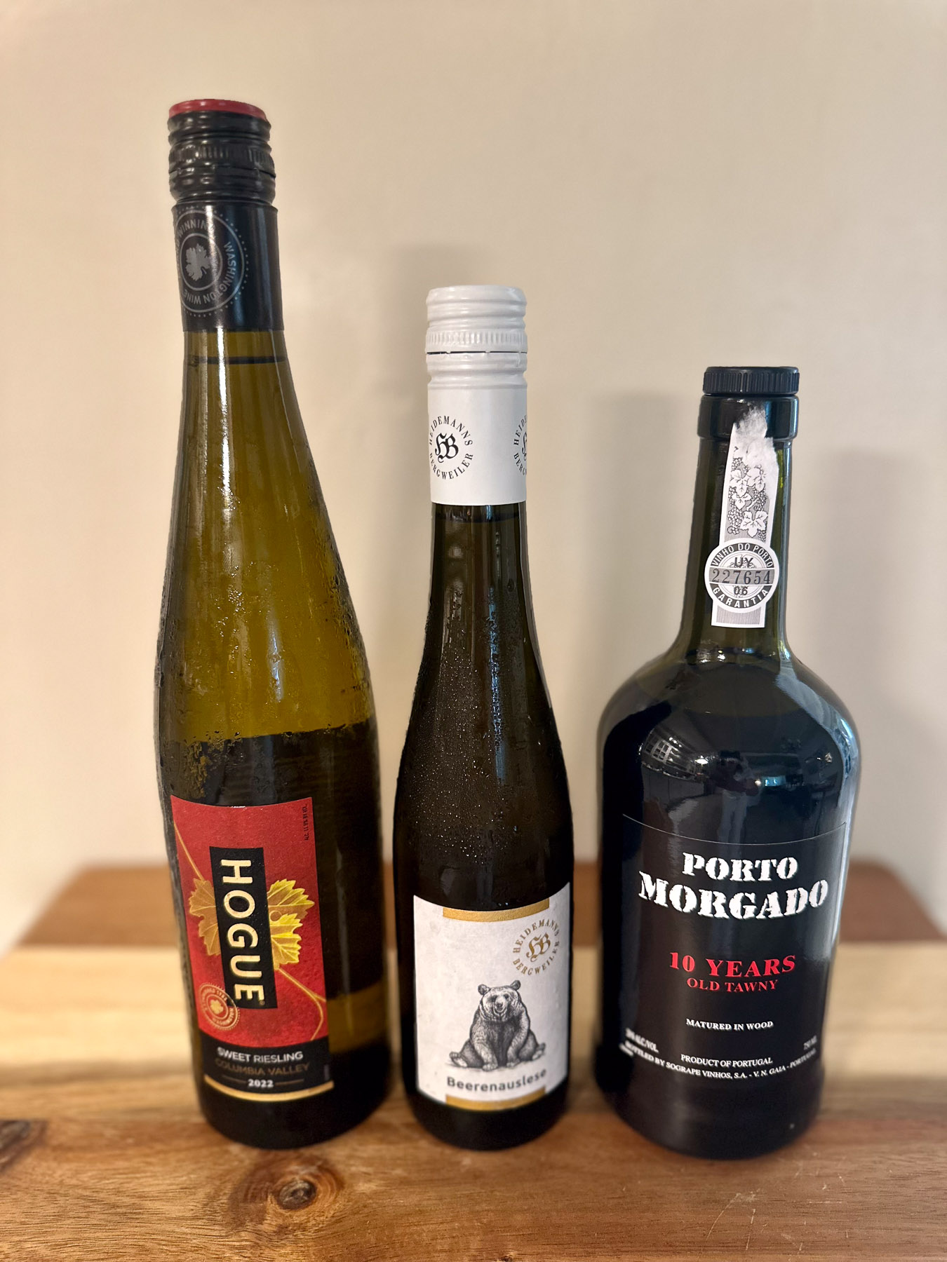 Three dessert wines displayed on a wooden table: Hogue sweet riesling, Dr. Heidemanns Beerenauslese, and Porto Morgado 10-year tawny port.