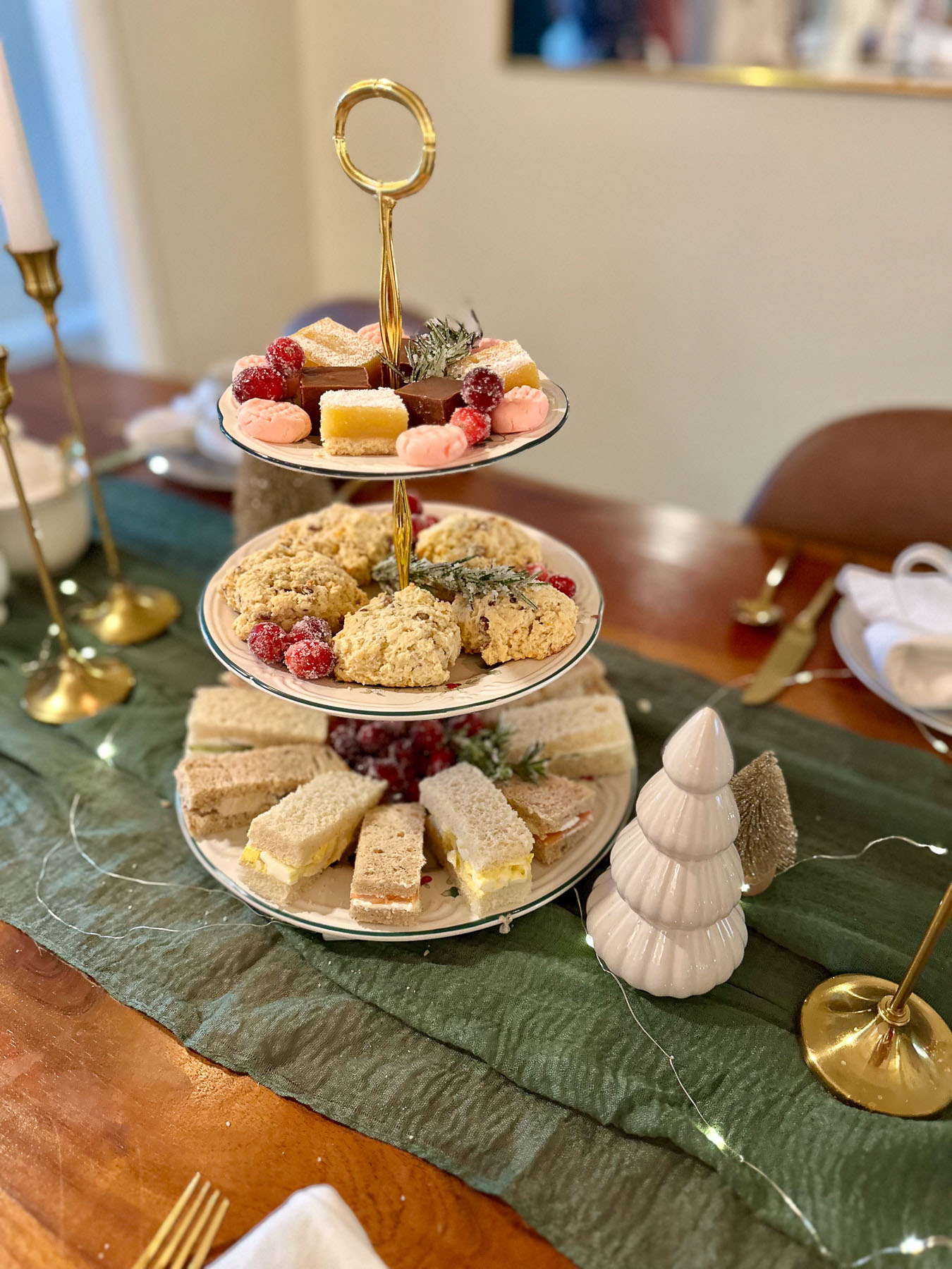 Three-tier serving tray with tea sandwiches, scones, and Christmas sweets on a festive table