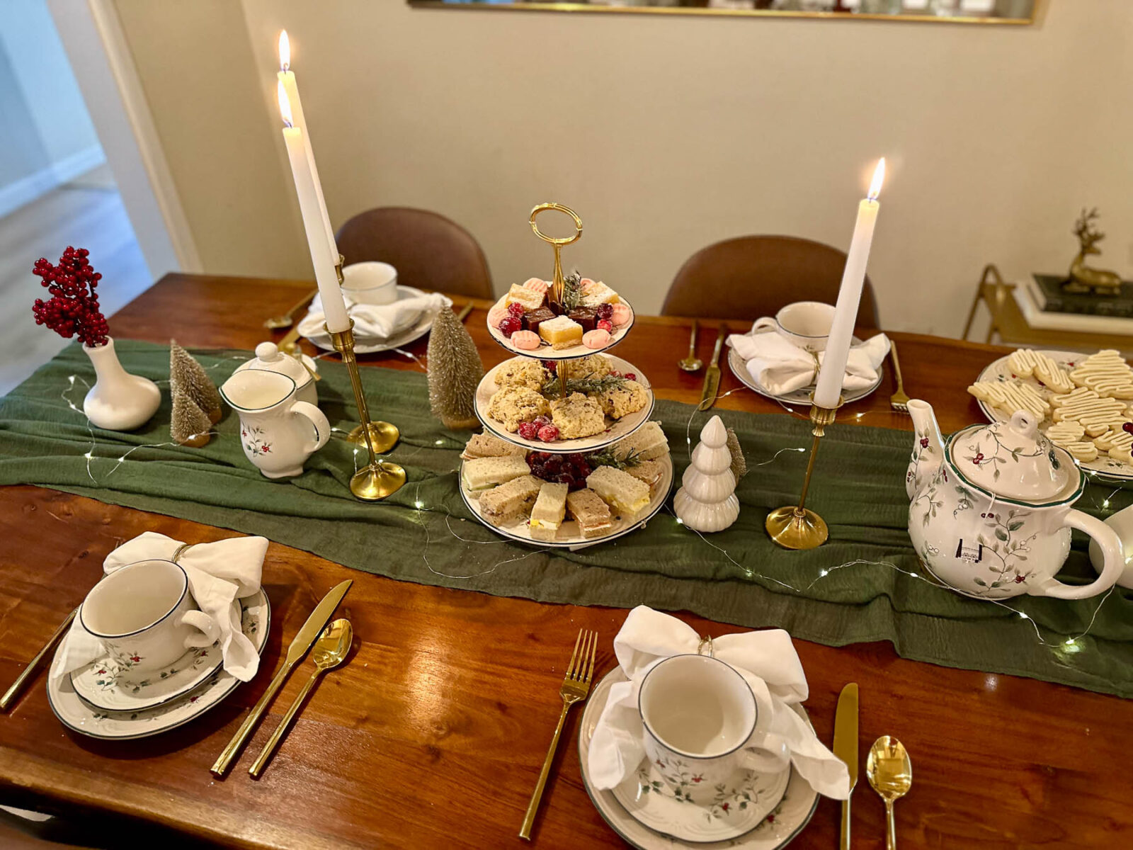 Festive Christmas tea party table set with teacups, tiered tray, candles, and green table runner