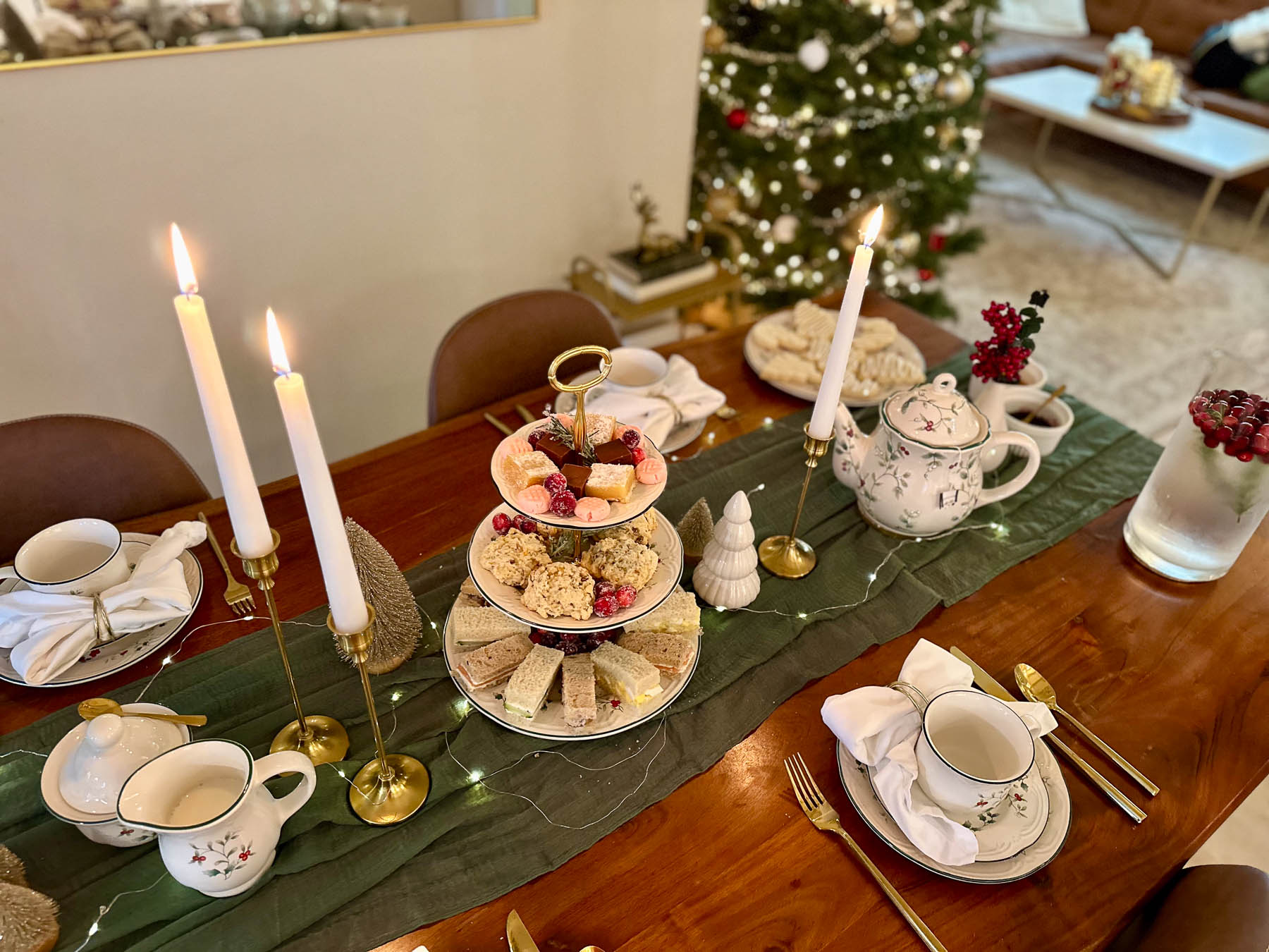 Christmas tea party table with tiered tray of tea sandwiches, scones, and sweets, set with festive teacups, candles, and holiday decor