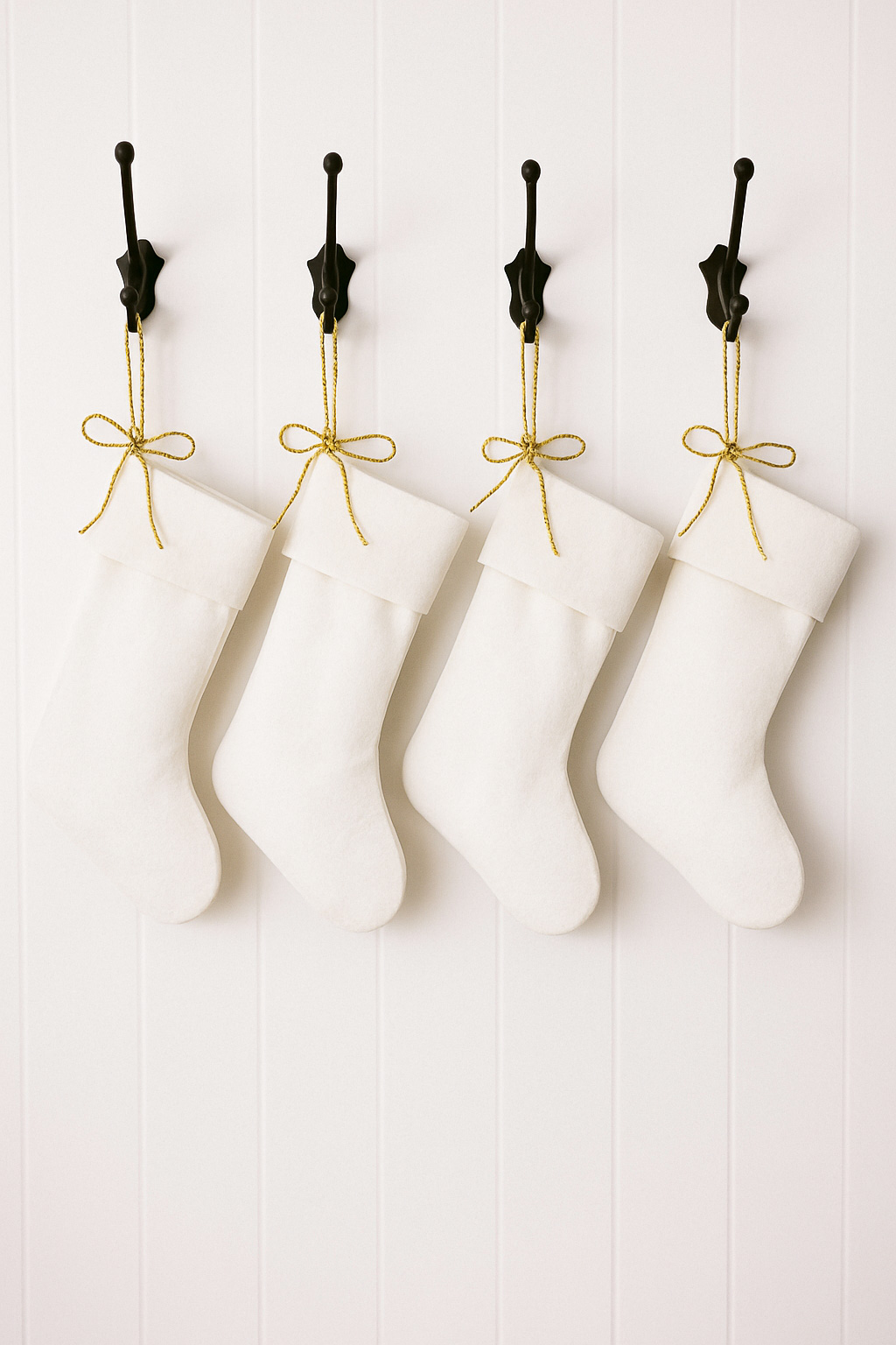 White Christmas stockings hanging from black wall hooks using gold ribbon