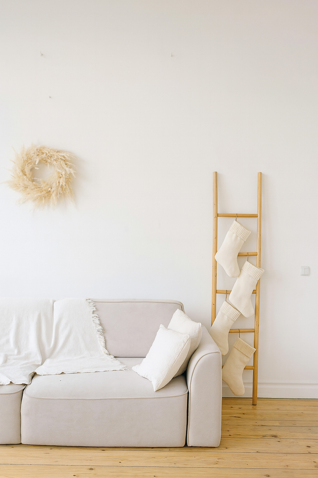 Neutral Christmas stockings hanging from a wooden blanket ladder next to a sofa