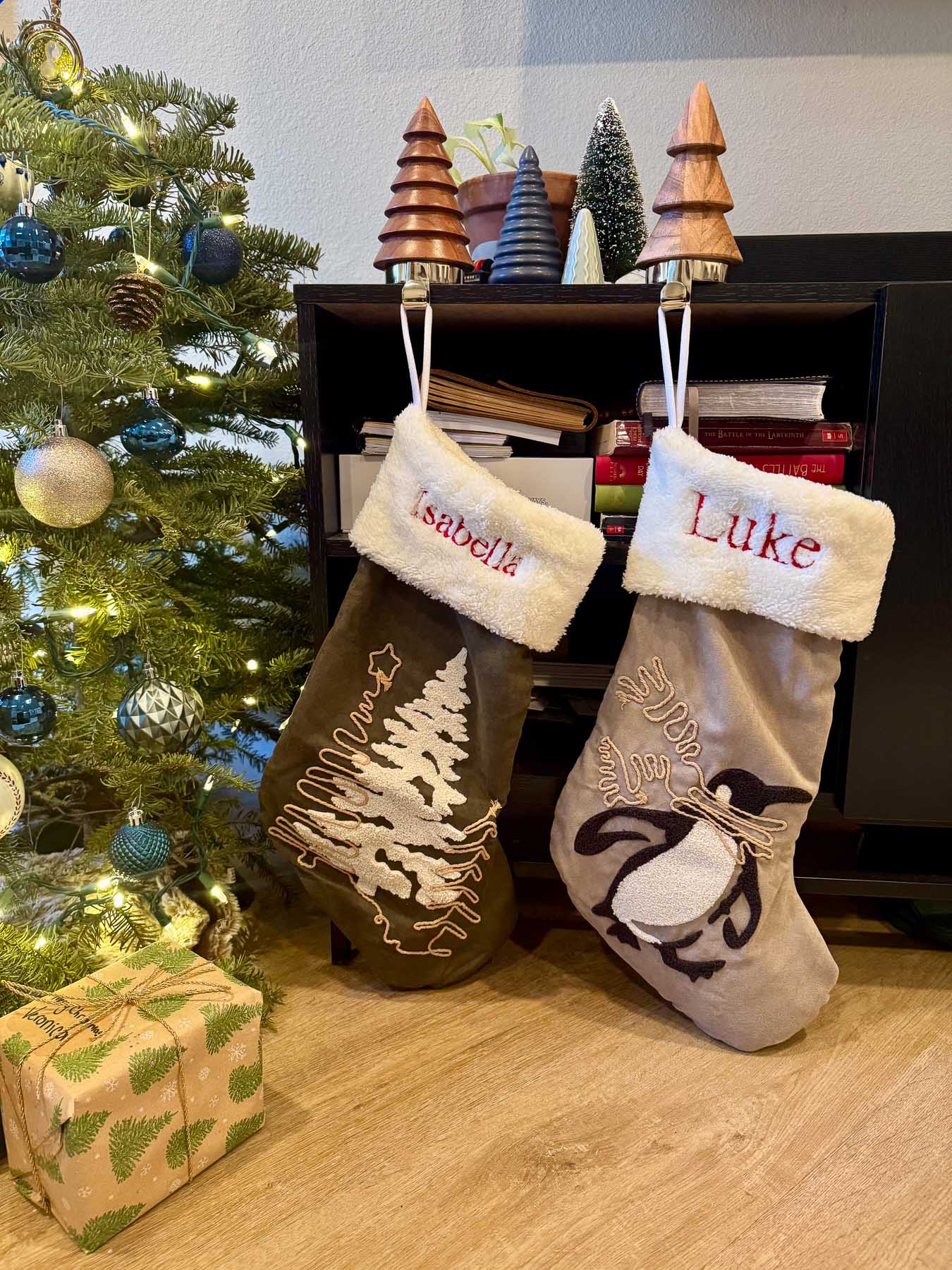 Two Christmas stockings hanging from a TV stand next to a decorated Christmas tree