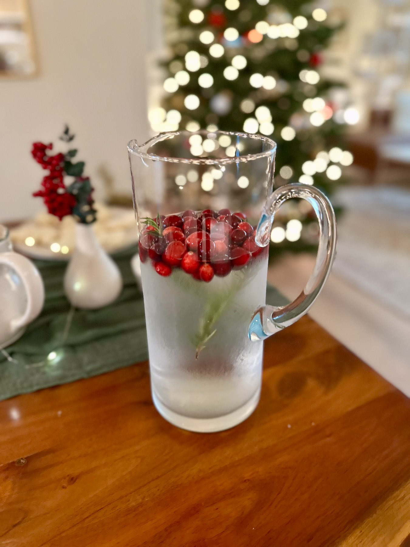 Glass pitcher with cranberries and herbs for a festive Christmas tea party drink station