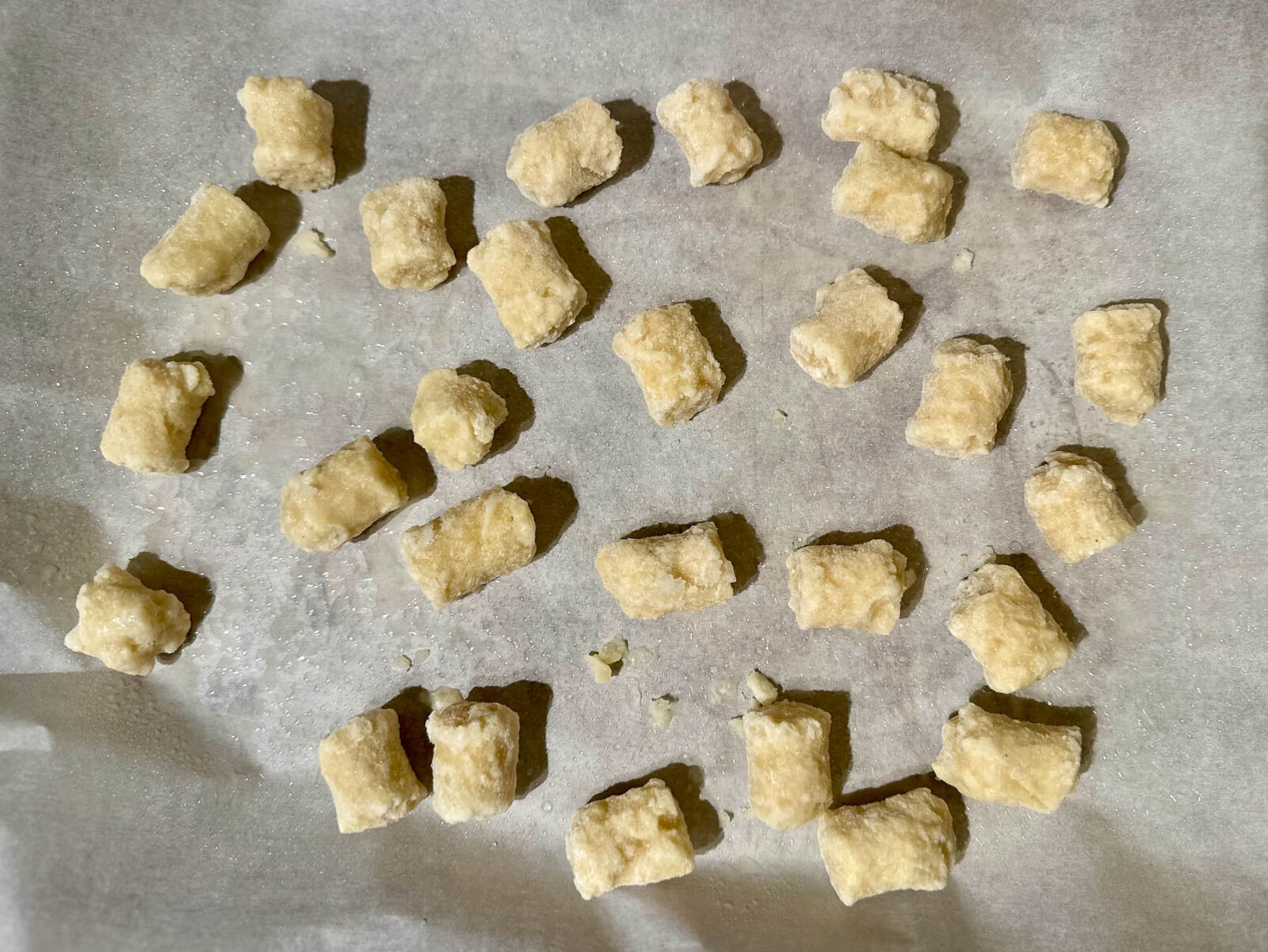 Frozen cauliflower gnocchi pieces spread out on a parchment-lined baking tray before roasting.